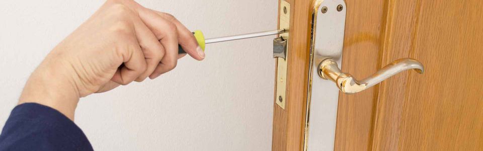 Hand using a screwdriver to adjust the latch on a wooden door
