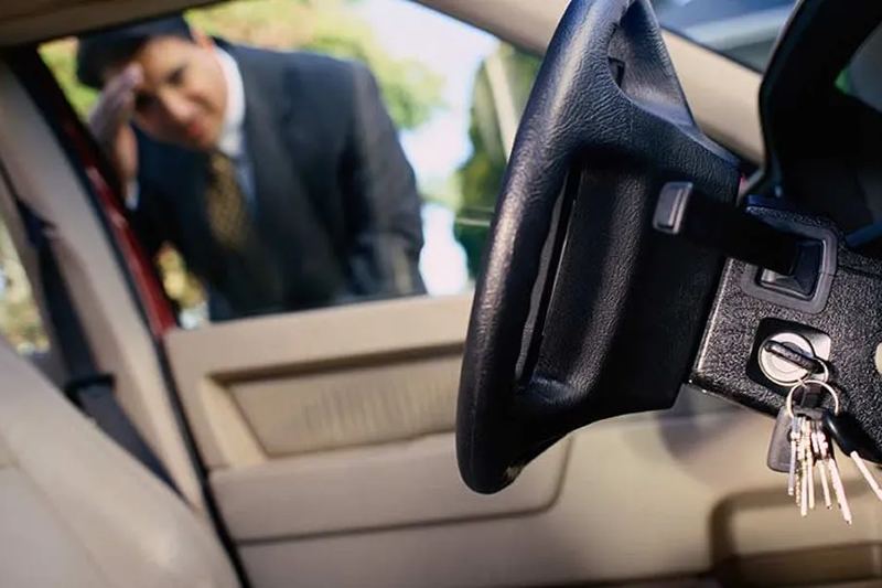 Man looking through a car window at keys left in the ignition