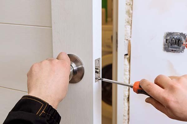 Locksmith using a screwdriver on a doorknob latch in a door frame