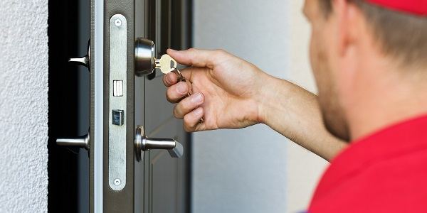 Locksmith in a red shirt turning a key in a door lock