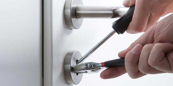 Locksmith using a screwdriver and pliers on a door handle and lock cylinder