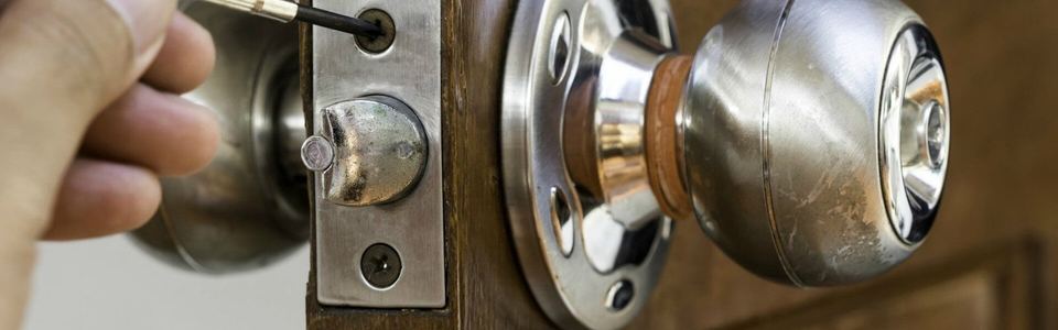 Hand removing a chrome doorknob and deadbolt from a wooden door